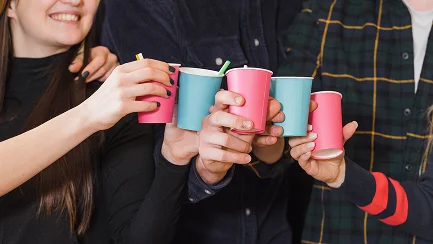 Detailní záběr na ruce přátel, kteří si připíjejí barevnými růžovými a modrými papírovými kelímky na večírku.